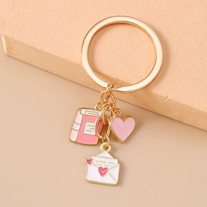 Detail of keychain featuring pink heart, book, and white envelope charms on gold ring
