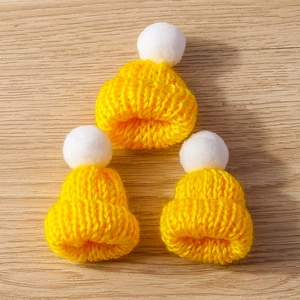Close-up of three yellow knitted mini hats with white pom-poms on a wooden background