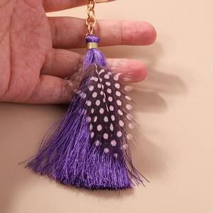 Elegant purple tassel and spotted feather keychain charm with gold metal clasp on beige background