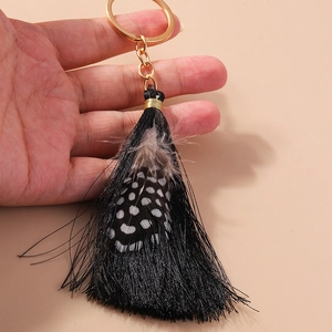 Close-up of bohemian tassel keychain with black silk fringe and a spotted feather detail