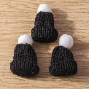 Close-up of three mini black knitted Christmas hats with white pom-poms on wood surface