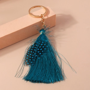 Detailed shot of peacock blue bohemian feather keychain with tassels on peach block