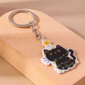Détail d'un porte-clés chat noir en acrylique avec guirlandes sur un support rose doux