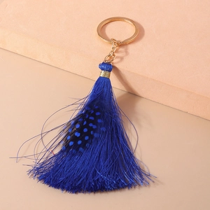 Close-up of royal blue tassel keychain with spotted feather on a soft pink background