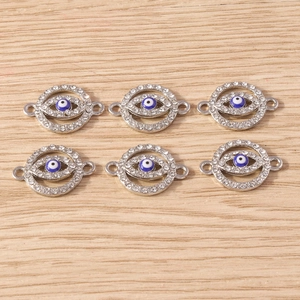Macro view of silver evil eye charms with white rhinestones and blue enamel inlay