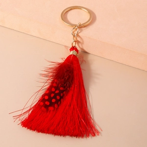 Detail of red tassel keychain with spotted feather and gold ring on beige stand