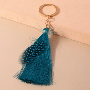 Detailed shot of peacock blue tassels and natural feather on a golden bohemian keychain