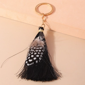 Detailed macro view of black tassel feather keychain with golden metallic ring loop