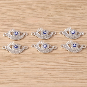 Detail showing silver evil eye connectors with rhinestones and blue enamel on wood surface