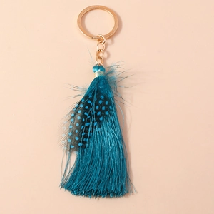 Detail of bohemian peacock blue feather keychain with soft silk tassels and gold metal ring