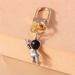 Detail of silver astronaut keychain with gold D-ring clasp on beige stone surface