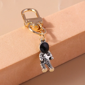 Detail view of retro silver astronaut keychain with gold carabiner on beige display