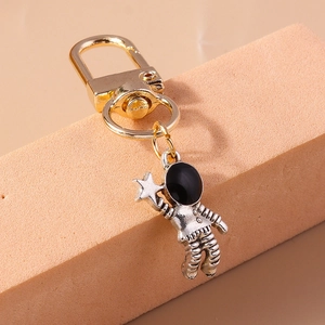 Macro detail of silver astronaut pendant with golden D-ring clasp on pink pedestal