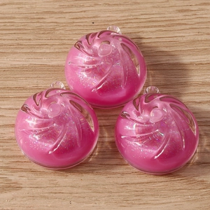 Close-up of three pink resin candy charms with glitter and swirls on a wood background