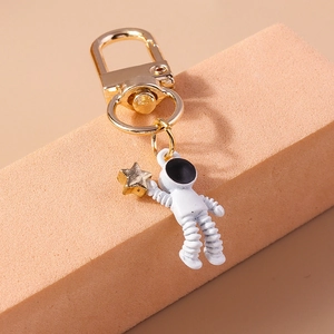 Close-up of a white astronaut keychain holding a gold star on an orange background