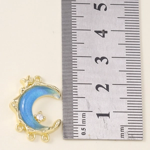 Detail showing crescent moon pendant with blue glitter and rhinestones next to a ruler