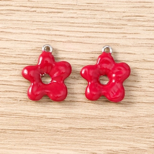 Detail of red flower-shaped metal pendants with silver loops on light wood surface