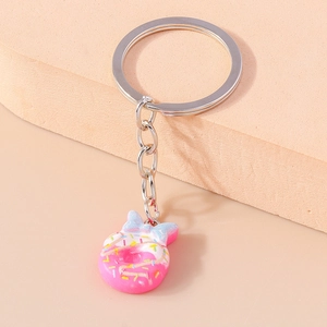 Close-up of pink donut keychain with blue bow and silver ring on geometric block
