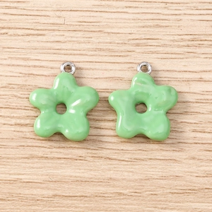 Detail of light green flower charms with silver rings on light yellow wood background