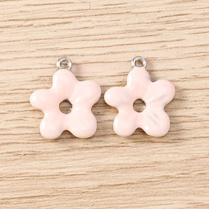 Pink enamel flower charms for DIY jewelry making on a light wooden background