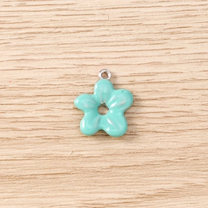 Detail view of mint green enamel flower pendant with silver loop on wood surface