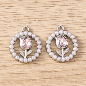 Detailed view of silver tulip charms with pink crystals and pearls on wood surface
