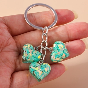 Gros plan de trois pendentifs cœur à paillettes vertes sur un anneau porte-clés poli