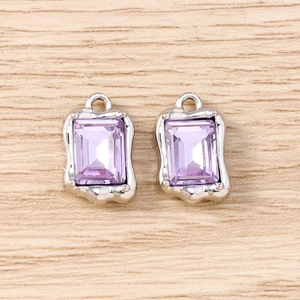 Detalle de dijes de cristal violeta con marcos plateados ondulados para joyería artesanal