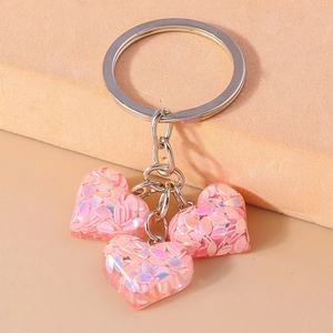 Gros plan sur des porte-clés cœurs roses aux paillettes irisées sur fond géométrique