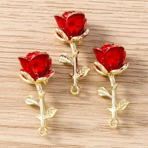 Detailed close-up of three red enamel rose pendants with gold stems on wood surface