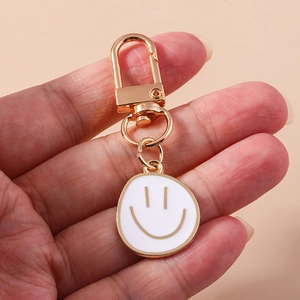 Porte-clés doré avec pendentif smiley en émail blanc tenu dans la main