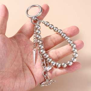 Silver beaded keychain with heart and punk spike charms shown in hand on beige background