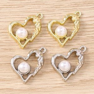 Dettaglio di ciondoli a cuore irregolare in oro e argento con perle su legno chiaro