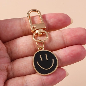 Gros plan du porte-clés smiley doré avec pendentif en émail noir tenu à la main