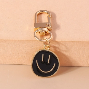 Détail d'un fermoir mousqueton doré avec un pendentif porte-clés smiley noir mat