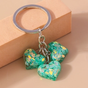 Détail de breloques cœur en résine verte avec paillettes irisées sur porte-clés argent