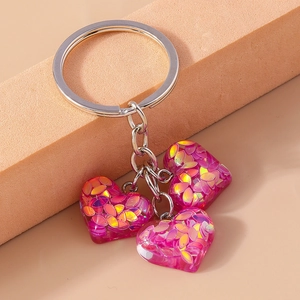 Détail macro de trois breloques cœurs en résine rose avec paillettes irisées sur anneau argent