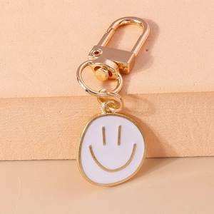 Détail d'un porte-clés smiley doré créatif avec émail blanc sur un fond de couleur pêche