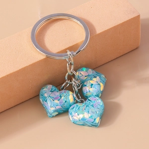 Détail de trois breloques cœurs à paillettes bleues sur un porte-clés en métal