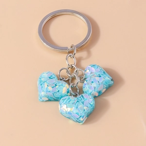 Détail macro de trois breloques cœurs bleu clair avec paillettes irisées sur porte-clés