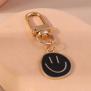 Détail d'un porte-clés visage sourire doré avec pendentif en émail noir et mousqueton