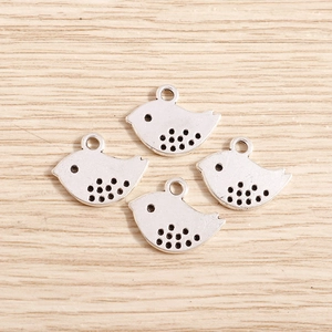 Close-up of four silver bird-shaped metal charms for DIY jewelry on a wood surface