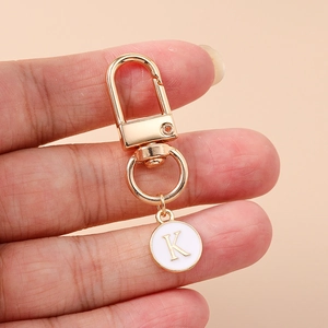 Detail of a gold letter K pendant keychain with white enamel and lobster clasp