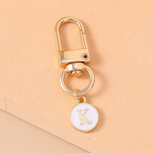Macro shot of gold metal keychain with white enamel round charm featuring letter K
