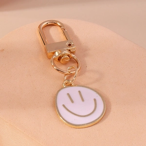 Gros plan d'un porte-clés visage souriant en émail rose avec crochet en métal doré