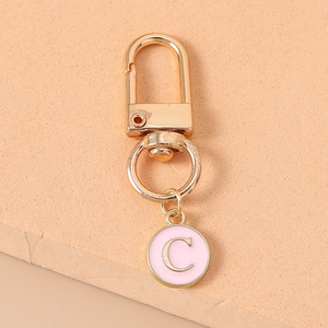 Detail of a gold lobster clasp with a pink enamel pendant featuring letter C engraving