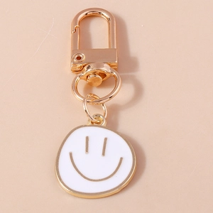 Détail d'un porte-clés doré avec pendentif smiley minimaliste et finition émail blanc