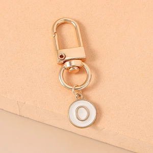 Detail of a golden metal keychain featuring a white enamel round letter O charm