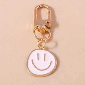 Détail d'un porte-clés en métal doré avec pendentif smiley en émail blanc et fermoir homard