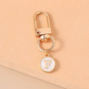 Close-up of gold metal letter F charm with white enamel on a polished keychain